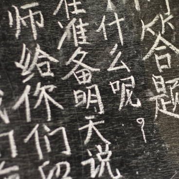 chinese1 girl writing Chinese characters on a blackboard at a remote school in Northern Thailand, Southeast Asia.